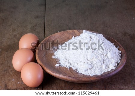 Eggs and flour in wooden plate on old oak table