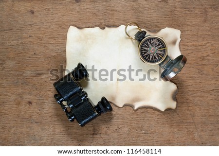 Compass, binoculars, grunge burnt paper on wooden texture background