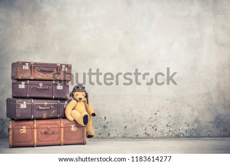 Teddy Bear toy with leather aviator\'s hat and goggles sitting on retro old aged classic travel suitcases circa 1940s. Travel luggage concept. Vintage instagram style filtered photo
