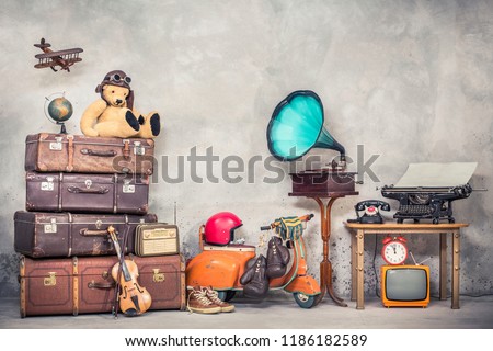 Retro Teddy Bear toy in aviator\'s hat, wooden plane, aged classic travel valises, globe, children pedal scooter, phonograph, typewriter, clock, TV, radio, old telephone. Vintage style filtered photo