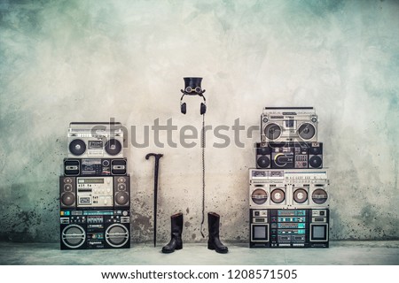 Retro old design ghetto blaster boombox radio cassette tape recorders, headphones, cylinder hat, leather boots, walking stick cane front concrete street wall. Vintage style filtered conceptual photo
