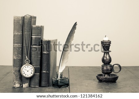 Old books, quill and inkwell, pocket watch, candlestick on wooden table