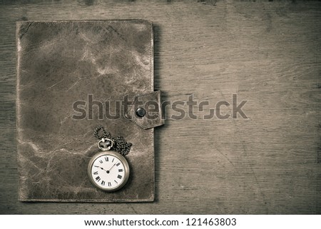 Old grunge leather notebook cover and pocket watch on grunge wooden table