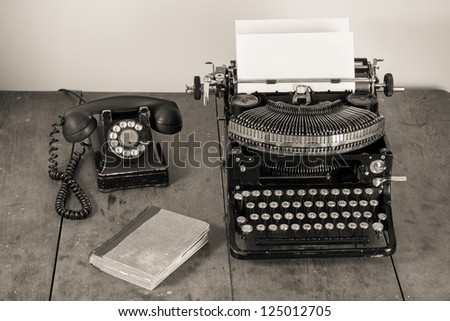 Vintage old typewriter, phone, book on table desaturated photo