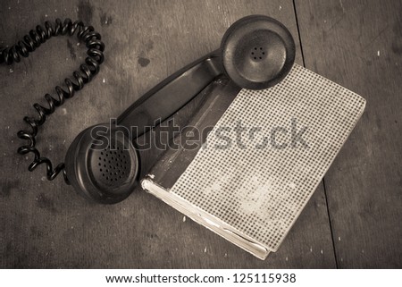 Old vintage phone handset, book on wooden table grunge background