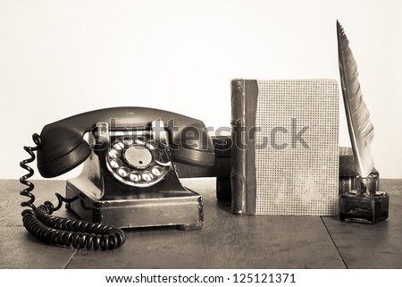 Vintage phone, old book, quill and inkwell on wooden table sepia photo