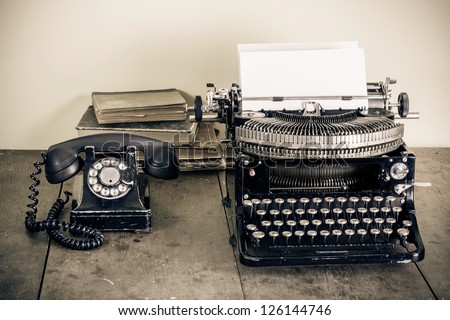 Vintage telephone, old typewriter, books on table desaturated photo