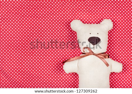 Handmade toy bear on red and white cotton background