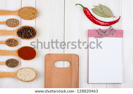 Recipe notebook, spices in wooden spoons on white wood background