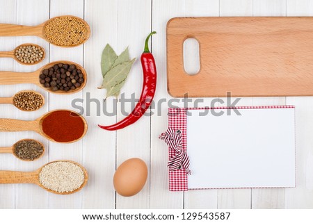 Recipe notebook, spices in wooden spoons on white wood background