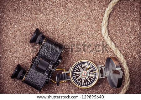 Vintage compass, binoculars on sand background