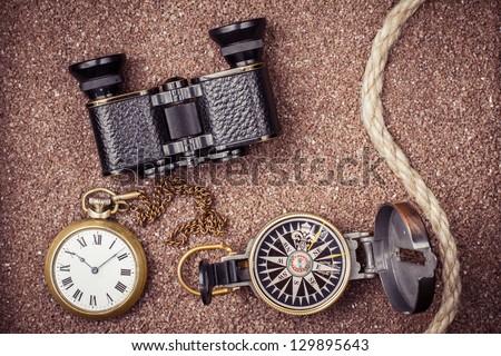 Vintage compass, binoculars, pocket watches on sand background