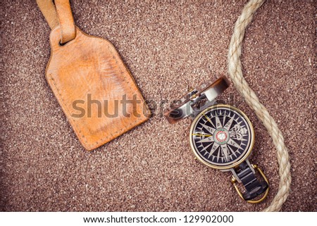 Vintage compass and leather tag on sand background