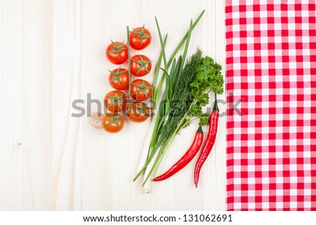 Red and white tablecloth, chili, green spices, cherry tomatoes on wood table background