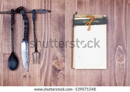 Old notebook, spoon, fork, knife on wood background