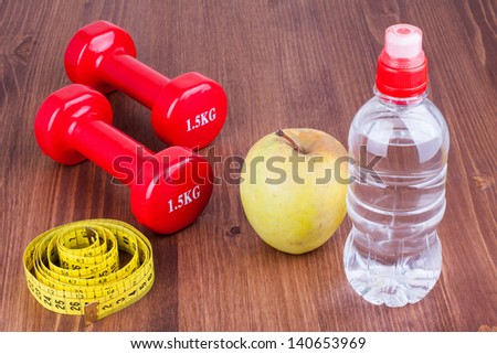 Fitness sport dumbbells, measure tape, apple, bottle of water on wood floor