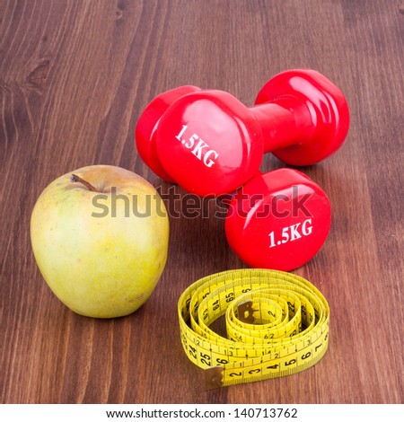 Red fitness sport dumbbells, apple, measure tape on wood