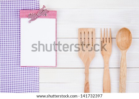 Tablecloth, recipe book, spatula, fork, spoon on white wood background