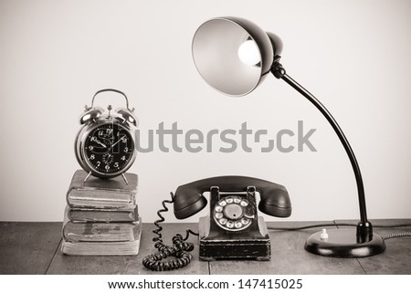 Old rotary telephone, table lamp, alarm clock, books still life