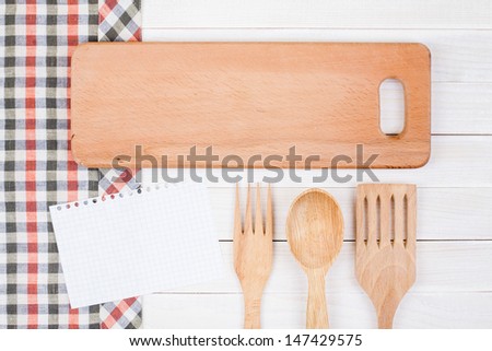 Kitchen cutting board, tablecloth, spatula, fork, spoon, note paper on white wood background
