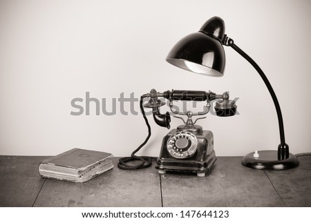 Vintage rotary telephone, old lamp, book on table