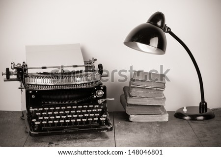 Vintage typewriter, old books and retro lamp on table