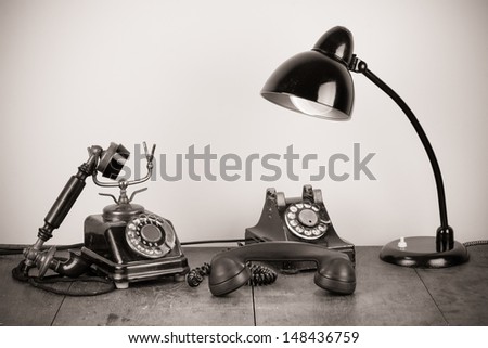 Old vintage rotary telephones and desk lamp on table sepia photo