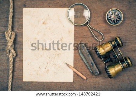 Compass, vintage binoculars, paper, old pocket knife, pencil, magnifying glass on wooden background