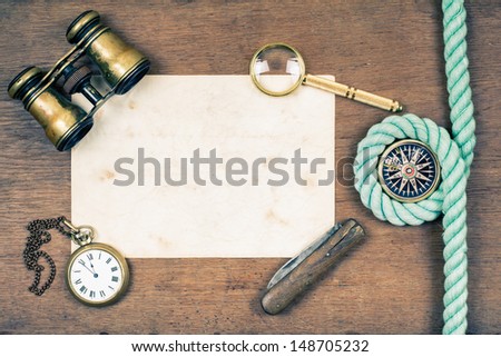 Vintage binoculars, compass, old paper, pocket watch, knife, rope, magnifying glass on wooden background