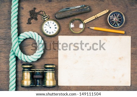 Vintage binoculars, compass, old paper, pocket watch, knife, pencil, rope, magnifying glass on wooden background