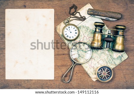Paper blank, vintage binoculars, compass, old map, magnifying glass, pocket watches, knife on wooden background