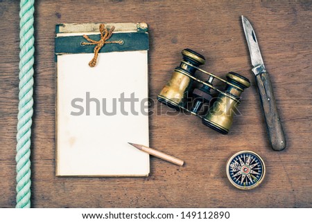 Vintage old notebook, binoculars, compass, knife, rope on wooden table background