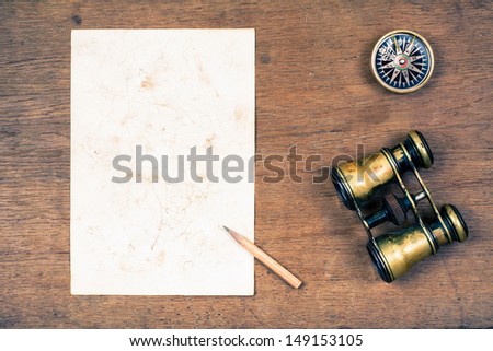 Compass, vintage binoculars, paper, pencil on wooden background