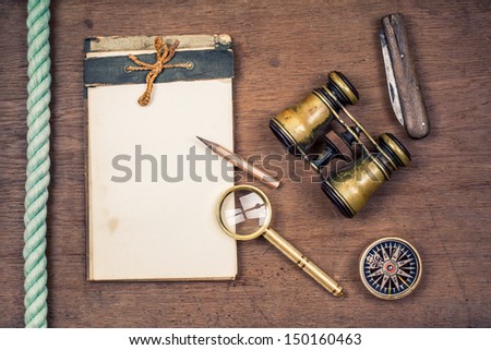 Vintage compass, binoculars, old notepad, pocket knife, pencil, magnifying glass, rope on wooden background