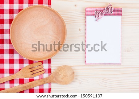 Red tablecloth, empty plate, notebook, spoon, fork on wood table background