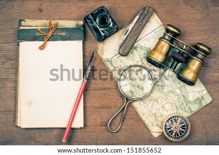 Vintage binoculars, notepad, compass, old map, ink pen, inkwell, pocket knife, magnifying glass on wooden background