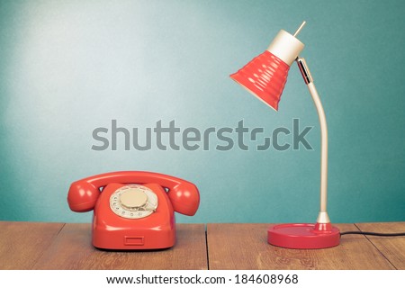 Retro red telephone and desk lamp on wood table front mint green wall background