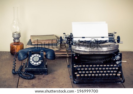 Vintage telephone, old typewriter, books, lamp on table
