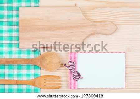 Recipe cook book, spoon and fork, kitchen board, tablecloth on wooden table