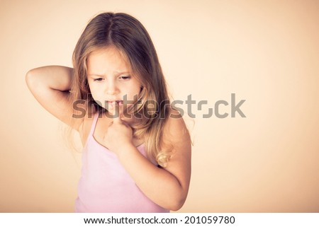 Little girl keeps finger near teeth and thinking about something. Retro style tinted photo