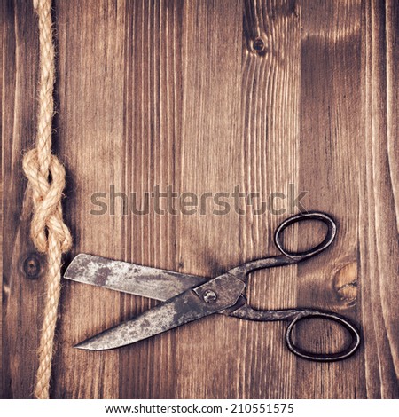 Vintage rusty scissors cut rope on old wooden background
