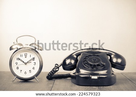 Retro old rotary telephone and alarm clock on table. Vintage style sepia photography
