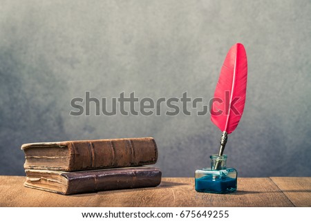 Vintage red quill pen with inkwell and old books on wooden table front concrete wall background. Retro instagram style filtered photo