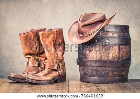 Wild West old retro leather cowboy boots, hat and oak barrel. Vintage style filtered photo