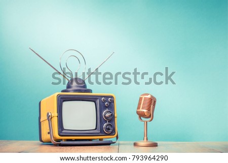 Retro old television receiver and golden microphone on table front gradient aquamarine wall background. Broadcasting concept. Vintage style filtered photo