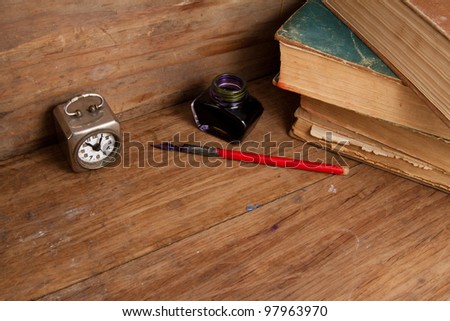 Antique clock, ink pen and inkwell, old books on wood background