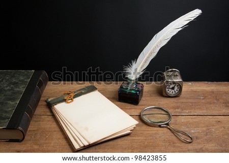 Old notepad, antique book, quill ink pen and inkwell, magnifying glass, vintage clock on wood table