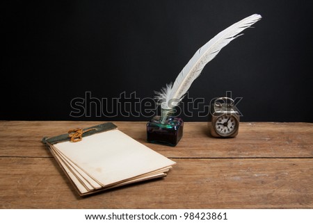 Quill ink pen and inkwell, old notepad, vintage clock on wood table