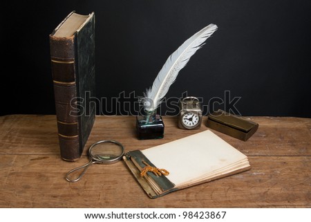 Antique book, magnifying glass, old notepad, quill ink pen and inkwell, vintage clock on wood table