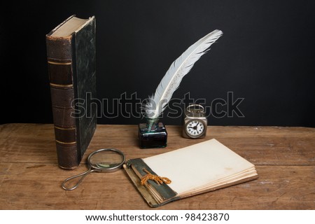 Antique book, old notebook, quill ink pen and inkwell, magnifying glass, vintage clock on wood table